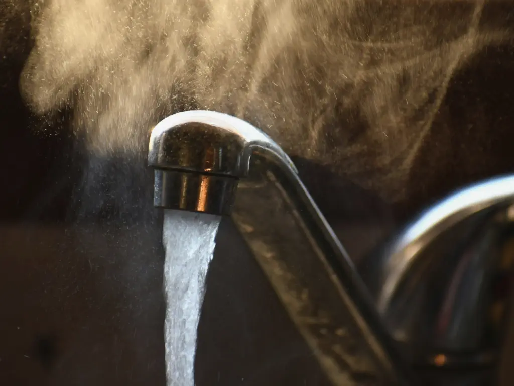 Mitigeur chromé d'où coule de l'eau chaude, vapeur qui s'élève à contre-jour