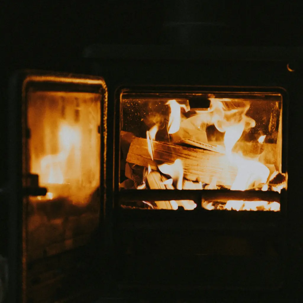 Poêle à bois en fonte au moment de l'allumage, porte vitrée entrouverte, flammes vives