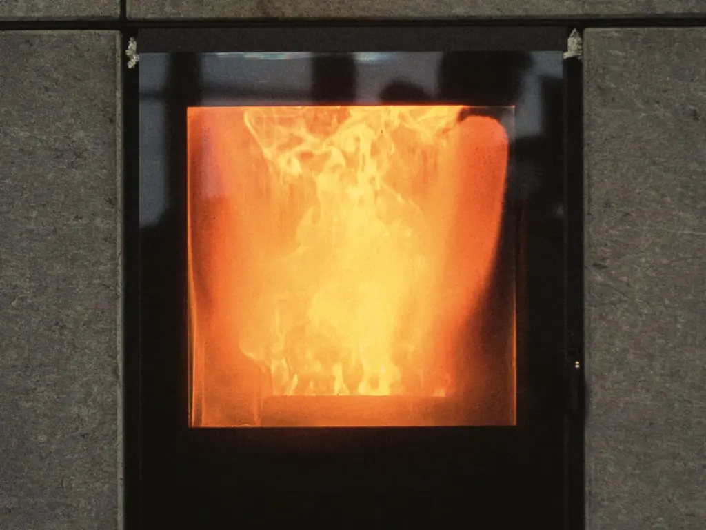 Flamme derrière la vitre carrée d’un poêle habillé de dalles de pierre grise