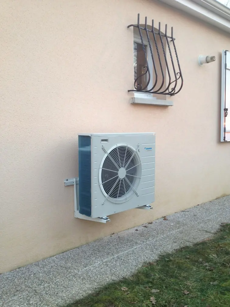 Unité extérieure de pompe à chaleur fixée sur une façade enduite, au-dessus d'une pelouse