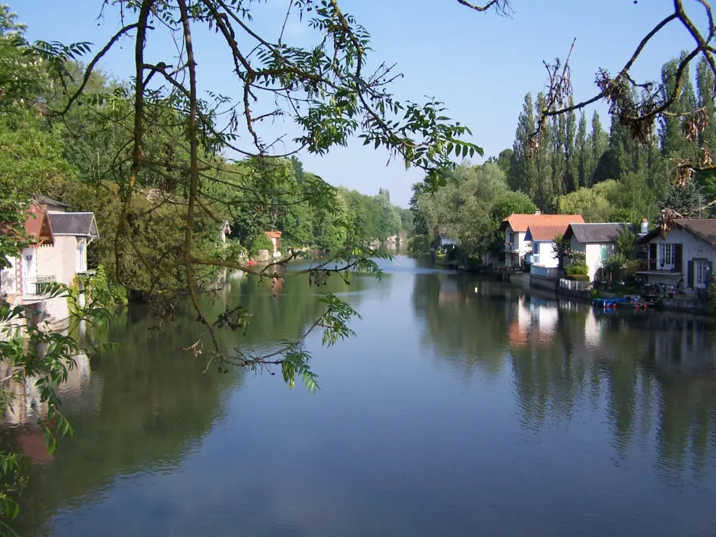 Le Loiret à Olivet : des maisons au bord de l’eau et leurs reflets, sous des branches d’arbre.